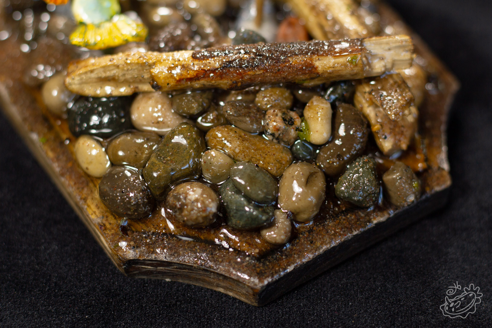 A close up on a model of a Brook Trout. The focus is on the resin coated sand, pebbles, and drift wood