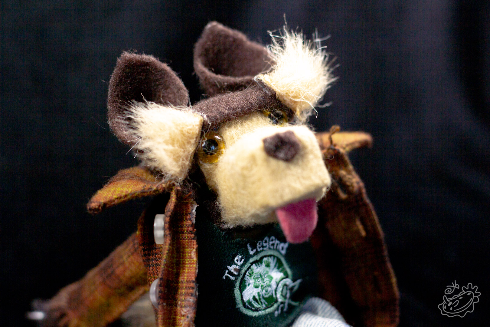 A felt doll of the Michigan Dogman. It is dressed in jeans, a band tank top with the art of the dogman on it, and a brown flannel. It is a close view of the face details.