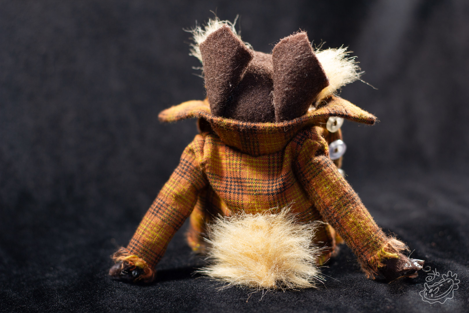 A felt doll of the Michigan Dogman. It is dressed in jeans, a band tank top with the art of the dogman on it, and a brown flannel. Rear View.